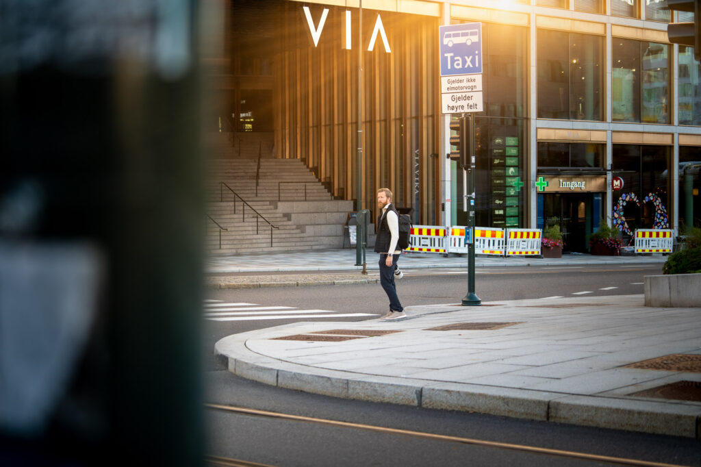 Bilde av en mann som står med kamera og tar bilder sentralt i oslo sentrum. Et glimt av sollys kommer fra høyre hjørne.