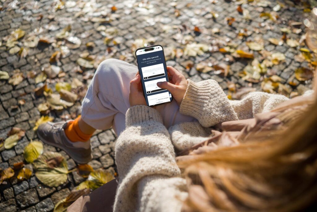 Bilde av en kvinne som sitter på en benk mens hun sitter på hjemmesiden til Klinikk haukeland gjennom sin mobiltelefon