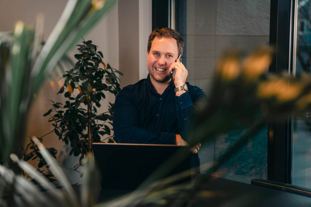 Bilde av Benjamin Lind Enger som smiler mot kamera mens han sitter i telefonen